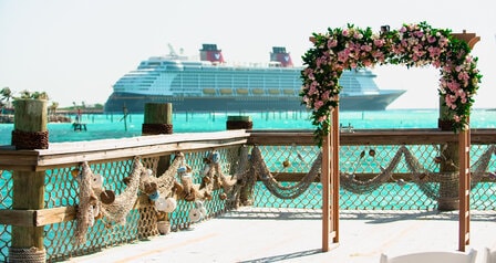 A wedding arch on a dock at Disney Castaway Cay with a Disney cruise ship docked in the distance
