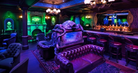 The Haunted Mansion Parlor featuring spooky décor, a tank with skeletal fish and a mirror above the bar with hitchhiking ghosts