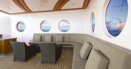 A lounge with a large, curved sofa, bar and chairs on the Disney Dream
