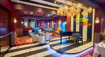 A woman playing the piano next to 2 bartenders at Scat Cat Lounge aboard the Disney Treasure