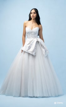 A bride wearing a Snow White inspired A line gown featuring a sweetheart neckline, a beaded bodice, floral designs and an off center bow at the waist