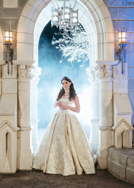 A bride wearing a Disney Fairy Tale Weddings 35th Anniversary Collection Belle inspired wedding gown featuring embroidery, an A line silhouette and a scoop neckline.