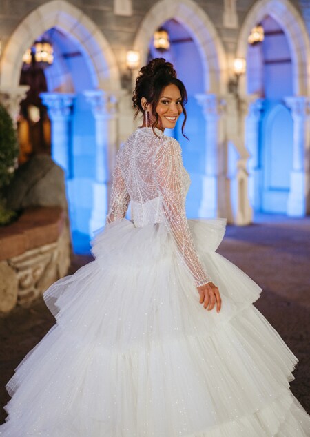 The back of a bride wearing a wedding gown featuring a tiered skirt and a beaded illusion top and sleeves