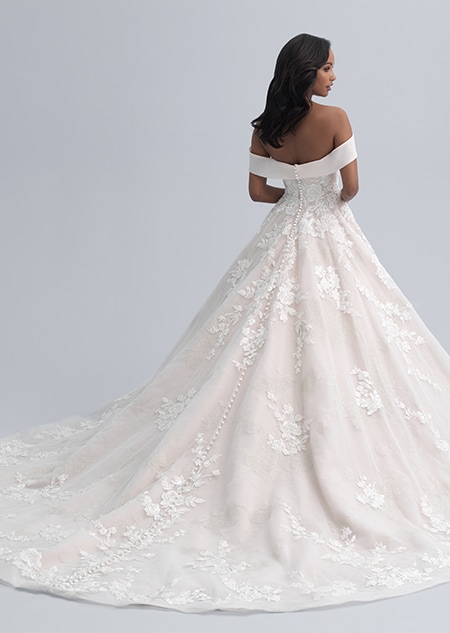 The back view of a bride in an off the shoulder dress with straps hanging above her elbows and a full skirt adorned with large flowers