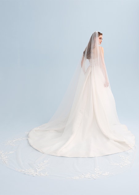 A woman looking over her shoulder wearing a wedding dress with a long and sheer veil