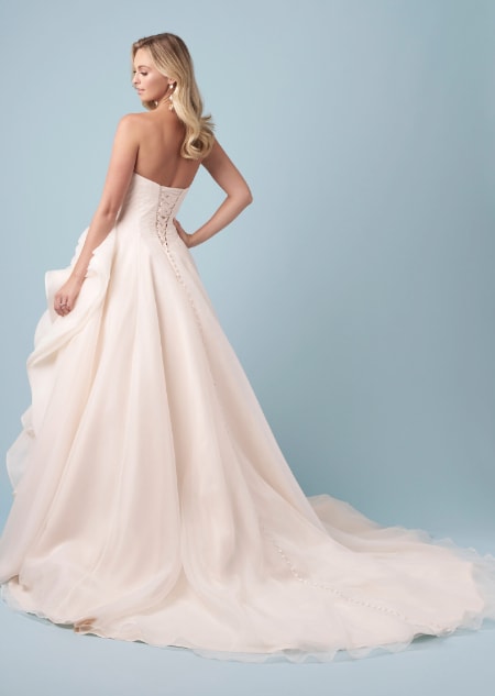 The back of a bride wearing a strapless Belle inspired A line wedding gown featuring a lace up back and a layered skirt gathered at the hip