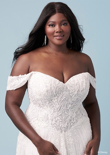 A bride wearing a Jasmine inspired sheath gown featuring off the shoulder sleeves, a sweetheart neckline and an embroidered bodice