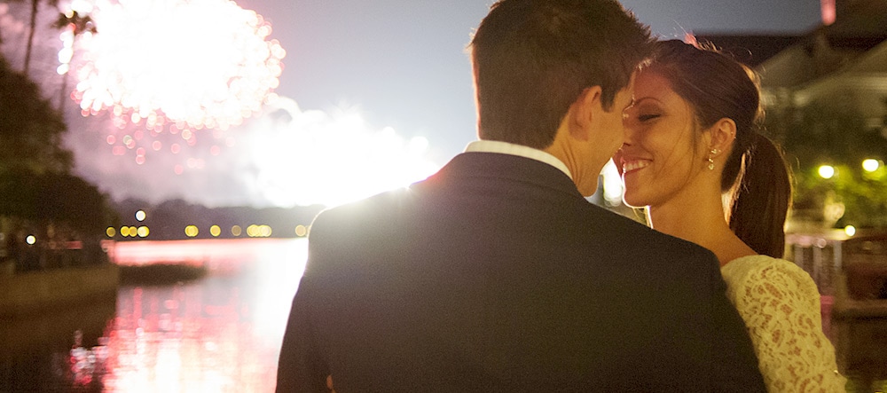 A man and woman lean in for a kiss during a fireworks display