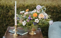 A bouquet of flowers inside a bronze vase, a book and a candlestick sitting on a wooden table