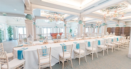 Chairs around a long table decorated with seashells and lanterns under ornate hanging decorations