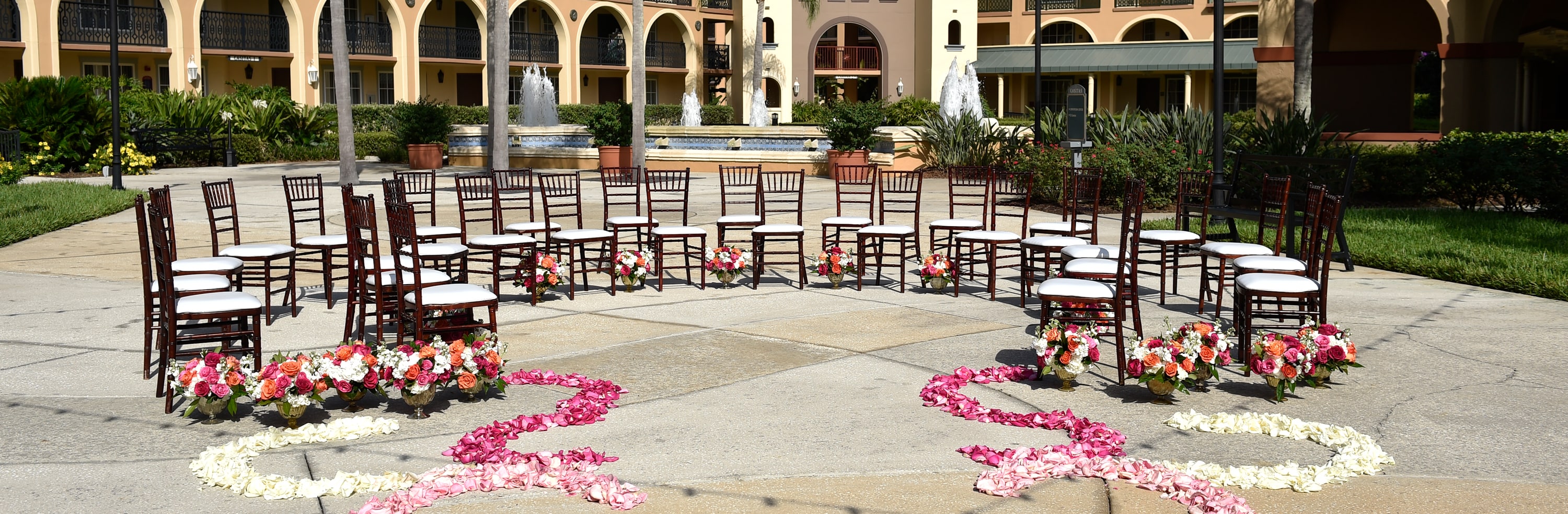 Rose petals lead to a group of chairs arranged in a semi circle on a courtyard with a large water fountain