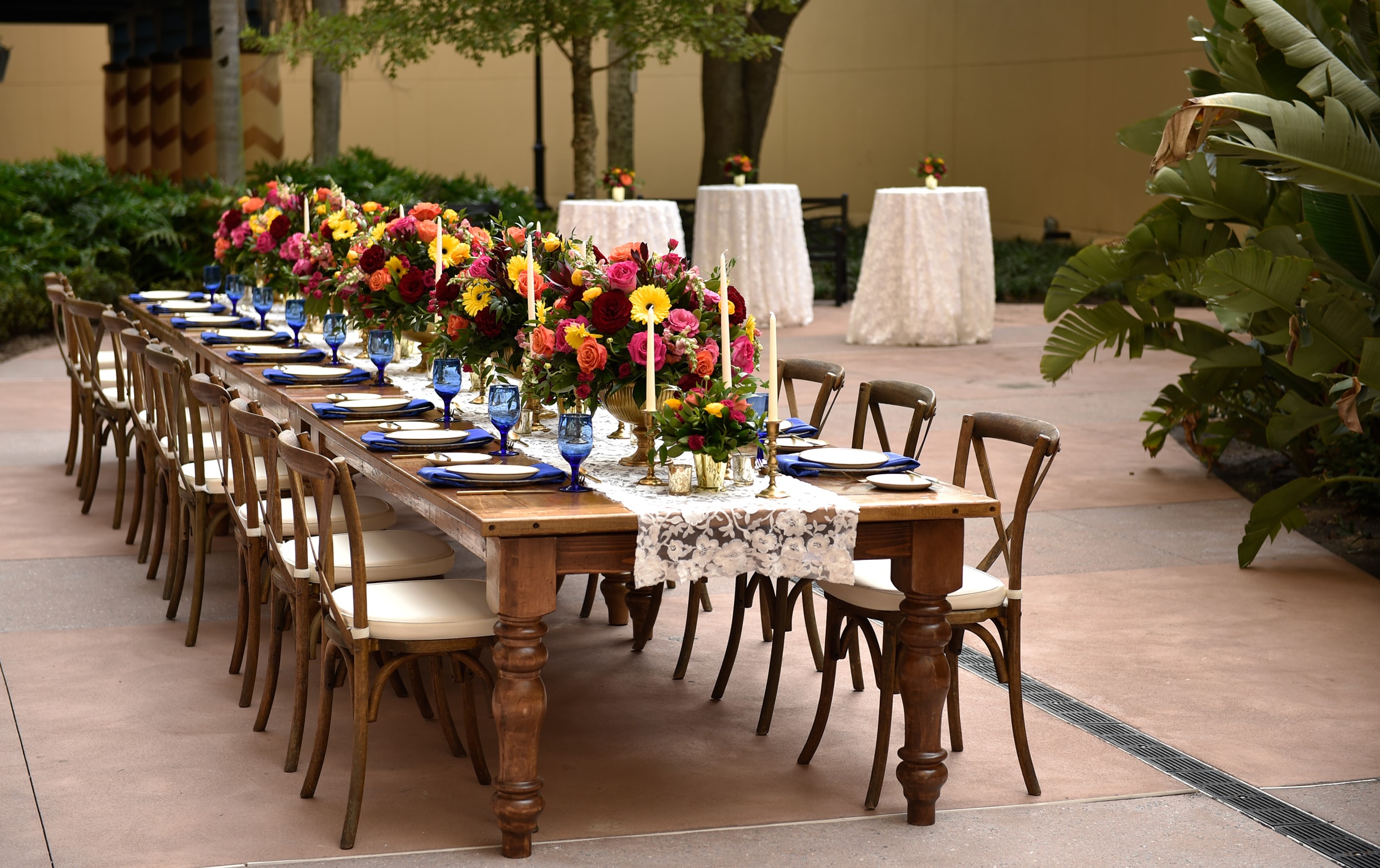 A long table with many place settings on a courtyard with 3 table tops in the background