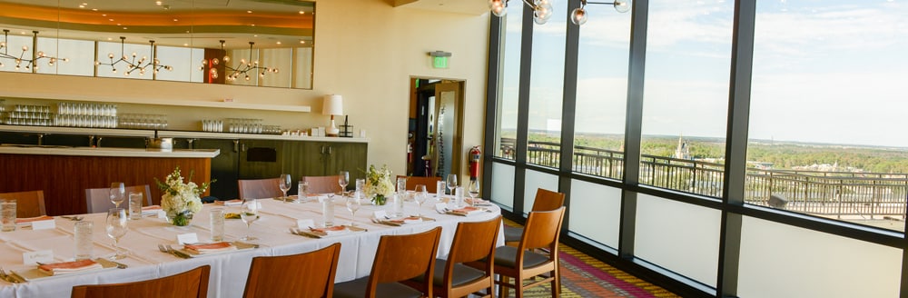 A long table set up near a bar and tall windows showing views of Cinderella Castle
