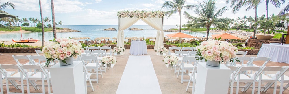 Two pillars holding rose bouquets line an aisle leading towards an altar outside