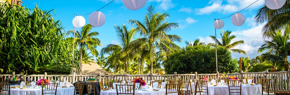 On a patio, paper lanterns are strung above tables set with floral centerpieces