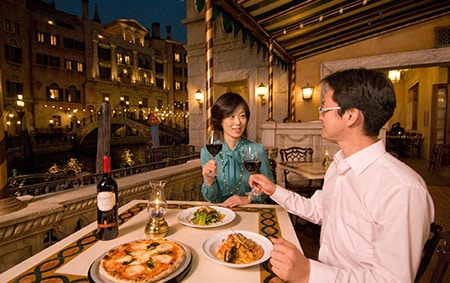 While seated at an outdoor dining table, a couple toasts each other before eating their meal
