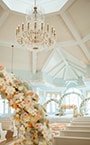 Disney's Wedding Pavilion, featuring pews, a vaulted ceiling, a chandelier, floral arches and flower petals strewn down the aisle