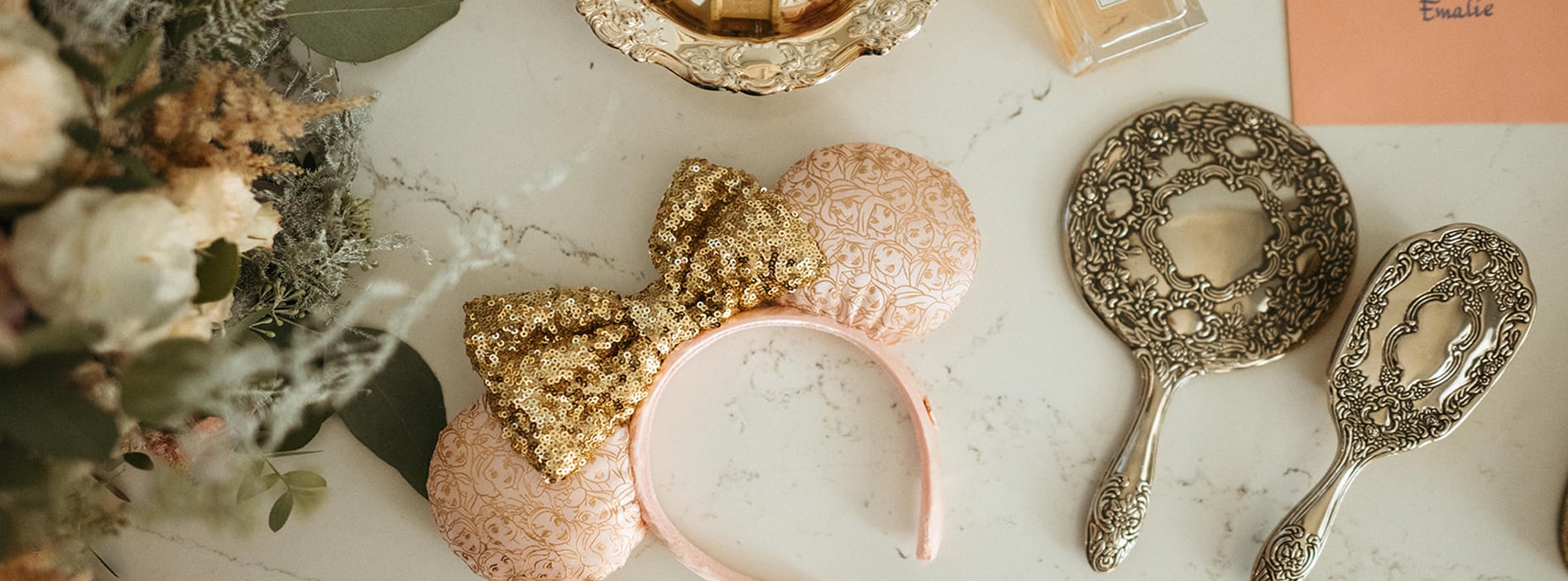 A table with a floral arrangement, a sequined Minnie Mouse ear headband and a silver hand mirror and hairbrush