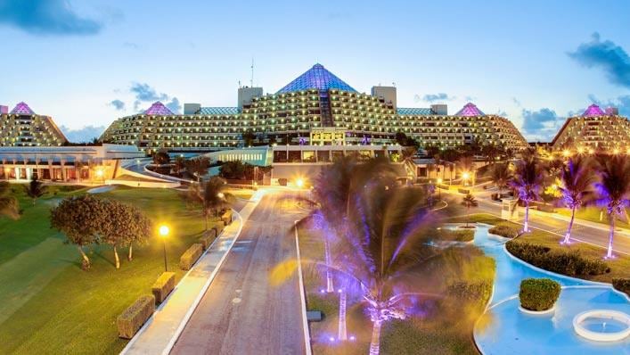 A road flanked by palm trees that leads to the entrance of a resort