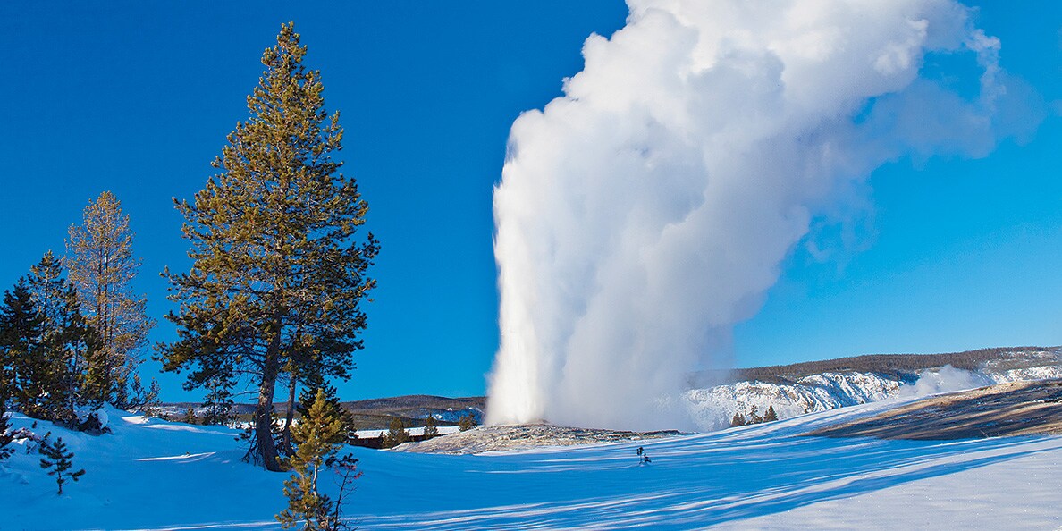 On a snowy terrain, a geyser sprays plumes of steam in the air