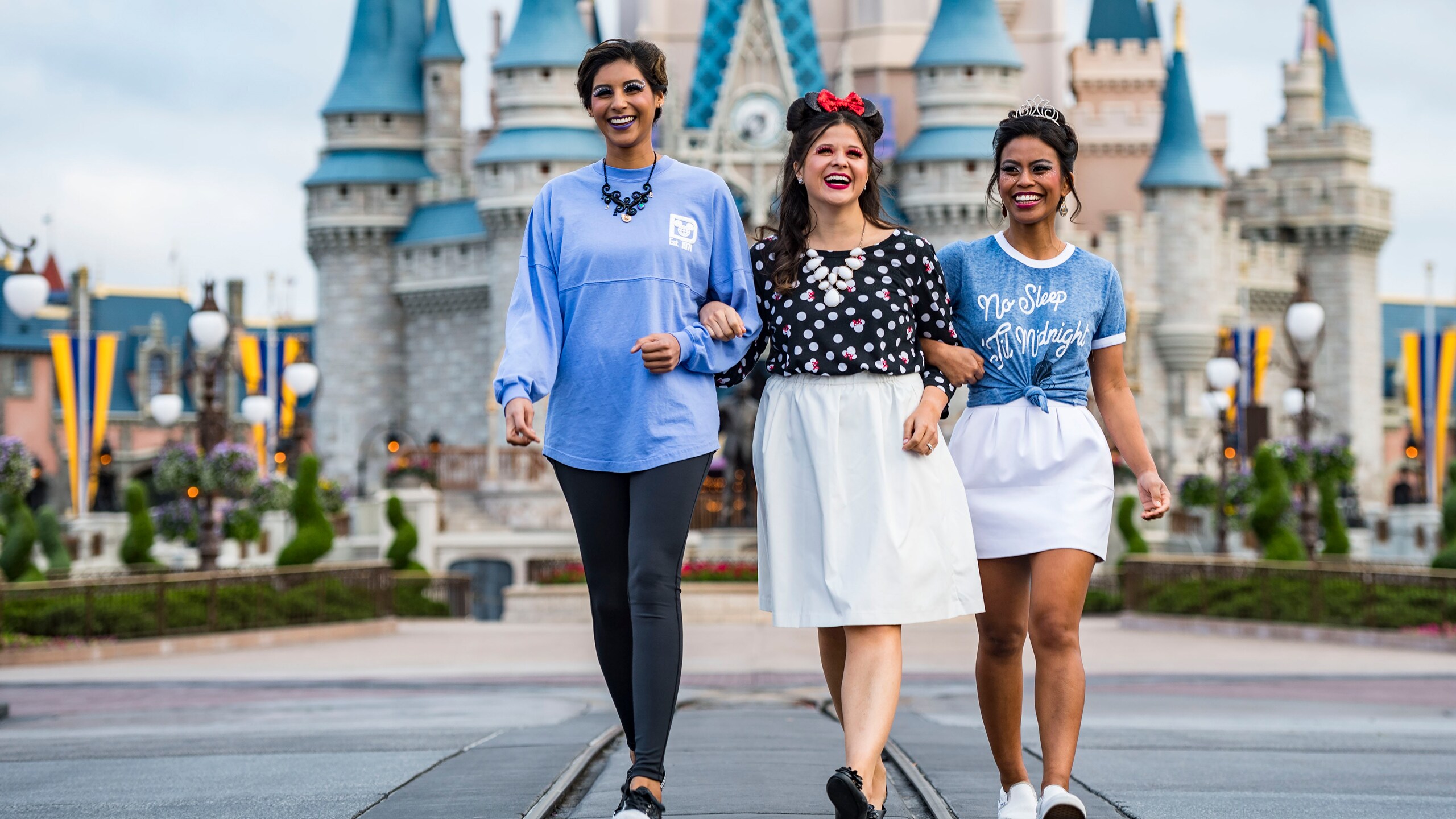 Three female Guests link arms while strolling in front of Cinderella Castle