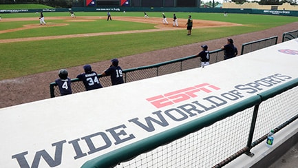 Varios jugadores en el campo de béisbol, junto a una pancarta que dice "ESPN Wide World of Sports Complex".