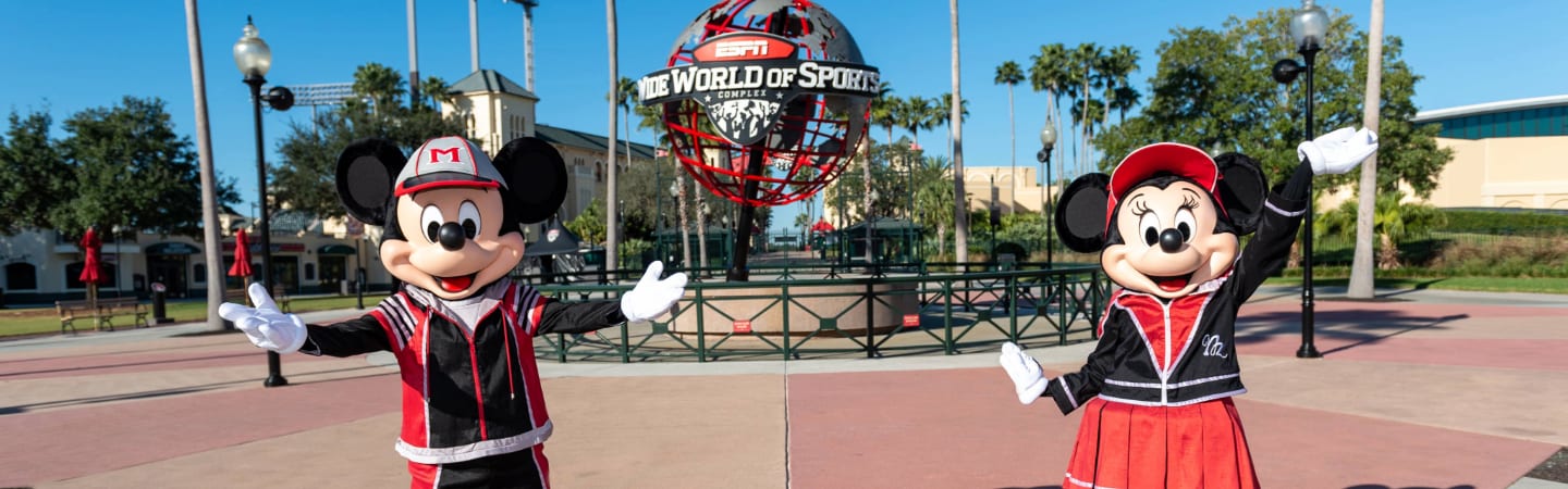 Minnie Mouse and Mickey Mouse standing near the ESPN Wide World of Sports Complex globe while dressed in sports themed attire