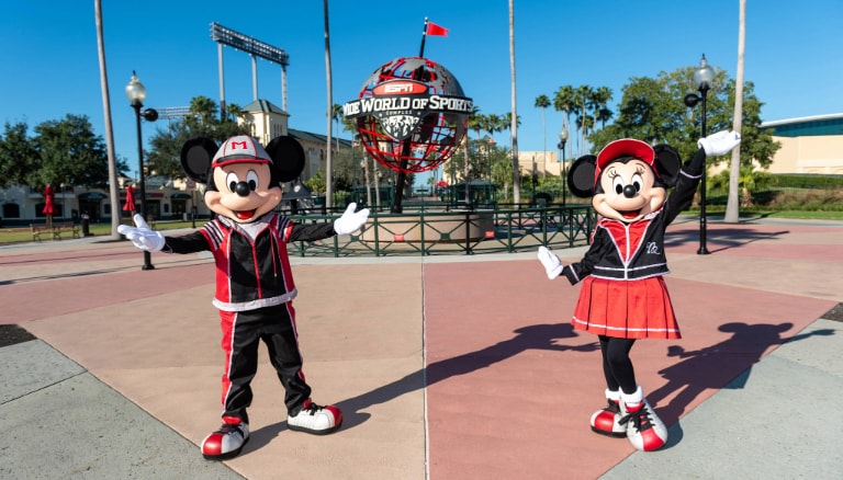 Minnie Mouse and Mickey Mouse standing near the ESPN Wide World of Sports Complex globe while dressed in sports themed attire