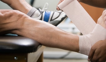 An athletic trainer wraps an athlete's ankle and foot