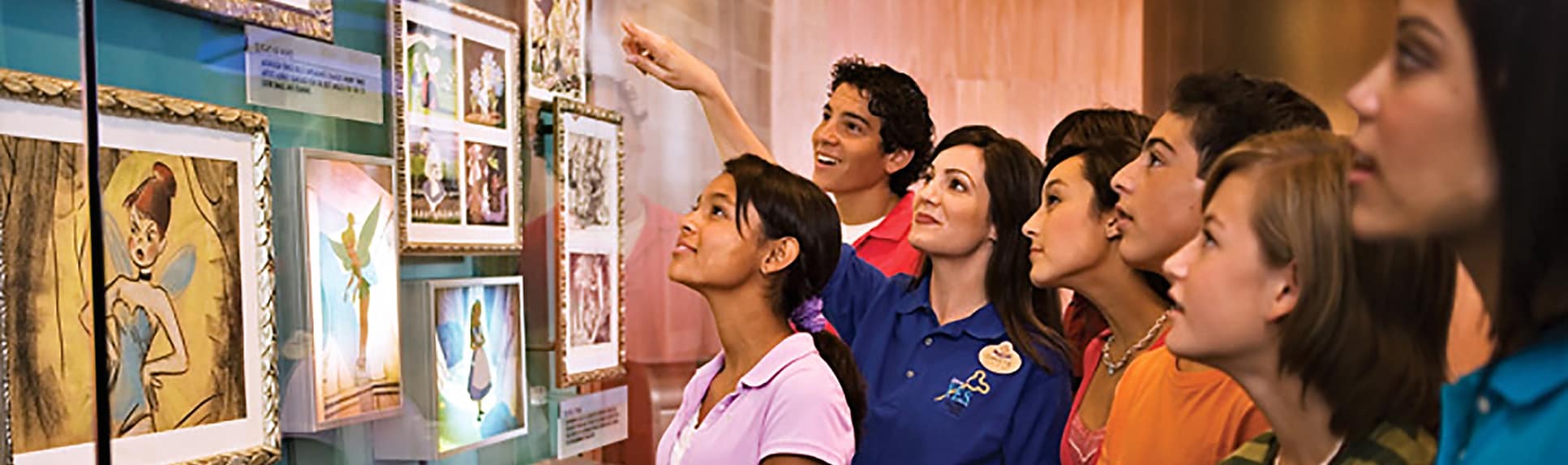 A Cast Member showing young adults Disney portraits encased in a glass display