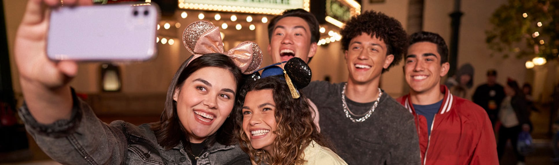 A group of 2 teen girls and 3 teen boys pose for a picture near Carthay Circle Theatre at night
